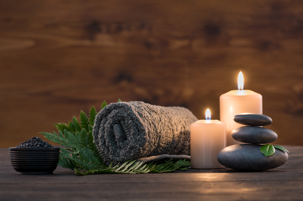 Stämnningsfullt stilleben med ihoprullad handduk, tända ljus och heta stenar som används vid massage